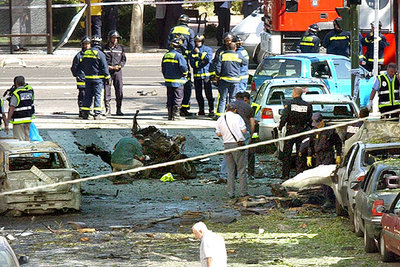Agentes de Información y de la Policía Científica recogen muestras del coche bomba que estalló ayer. Al fondo, tras los bomberos, la marquesina de Alcalá junto a la que cayó el capó del coche.