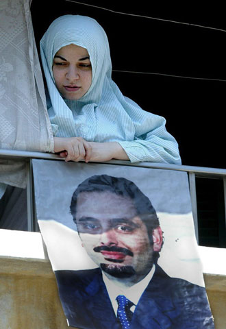Una mujer se asoma a un balcón con un cartel del hijo de Hariri.