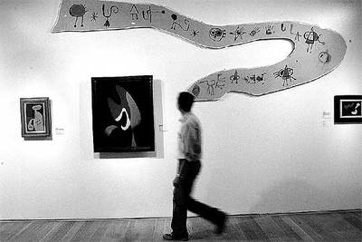 Un hombre camina frente a  Friso para la Exposición Internacional del Surrealismo (superstición-serpiente) , de Joan Miró (1947), expuesta junto a obras de Kurt Seligmann y René Magritte.