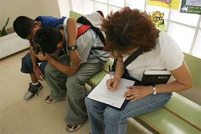 Un amigo consuela a Michael en el instituto mientras la agente tutora rellena la ficha con los datos del muchacho.