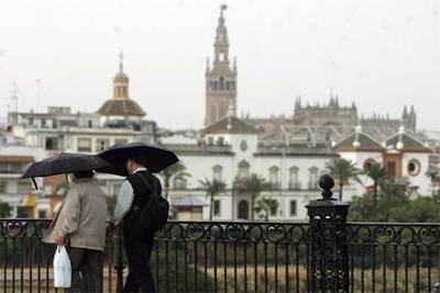 Dos transeúntes cruzan bajo la lluvia el puente de Triana, en Sevilla.