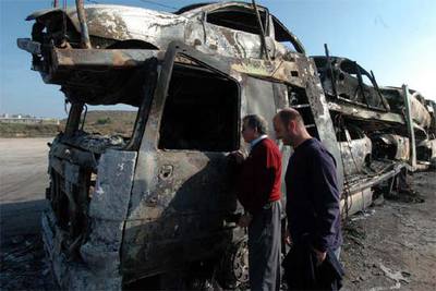 Dos personas observan un camión cargado de turismos quemados en la localidad de Peñalba.