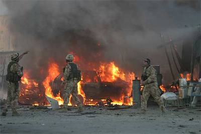 Soldados de la OTAN, junto a uno de los vehículos incendiados tras la explosión ayer de un coche bomba.