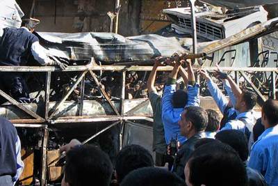 Bomberos iraquíes intentan quitar el techo del autobús que un terrorista hizo estallar ayer en Bagdad.