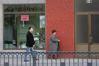 Pilar Elías, viuda de Ramón Baglietto, acompañada de un escolta, pasa por delante de la cristalería Aldako.