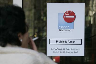 Una mujer fuma en la entrada del Ministerio de Industria, en Madrid, ante un cartel que prohíbe fumar en el interior.