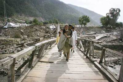 Un paquistaní traslada a una mujer herida en un puente de Balakot tras el terremoto del pasado octubre.