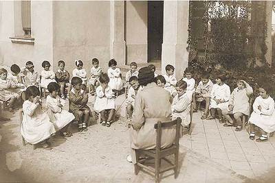 Una maestra con sus alumnas en la época de la II República. A la derecha, carteles de la FETE alusivos a la tarea del profesorado y a la educación infantil.