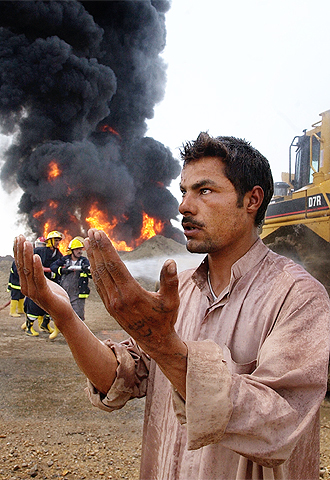 Un iraquí reza mientras unos bomberos intentan extinguir el incendio de un gasoducto en Diwaniya.