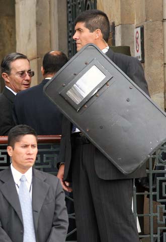 Álvaro Uribe entra en el edificio del Congreso bajo la estricta vigilancia de su equipo de guardaespaldas. En la pared, un cartel prohíbe entrar con armas en la sede legislativa.
