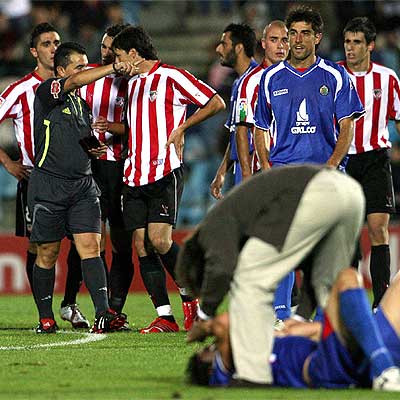 Un jugador del Getafe es atendido en el césped mientras los futbolistras del Athletic protestan al árbitro.
