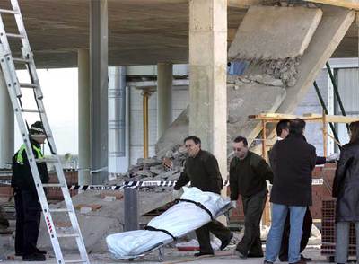 Dos operarios del retén fúnebre retiran uno de los dos cadáveres aplastados por el desplome de una escalera de hormigón en Algemesí.