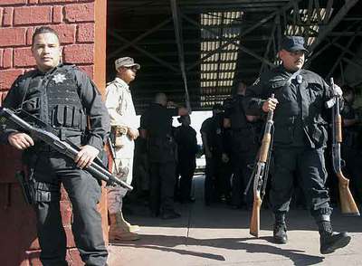 Un oficial de la policía local sale, cargado con dos fusiles, del cuartel general de Tijuana, vigilado por el Ejército y la policía federal.
