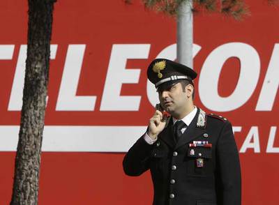 Un  carabiniere  habla por su teléfono móvil a las puertas de la sede de Telecom Italia en la ciudad de Rozzano.