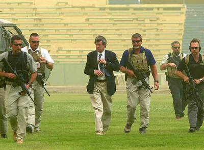 Guardaespaldas privados protegen al antiguo  virrey  de EE UU Paul Bremer (centro) a la llegada de éste al estadio de Bagdad para felicitar a los futbolistas por su clasificación para los Juegos de Atenas, en junio de 2004.