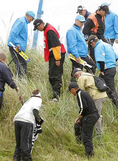 Mickelson, en el centro con un peto, busca la bola que falló en el segundo hoyo.
