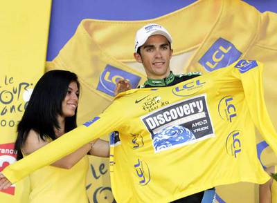 Una azafata ayuda a Alberto Contador a enfundarse el  maillot  amarillo tras el término de la etapa.