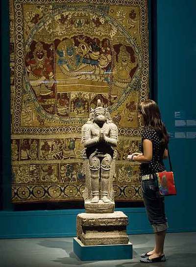 Escultura del dios mono Hanuman, del siglo XVI, ante un tapiz con escenas del  Maha-Bhaarata.  