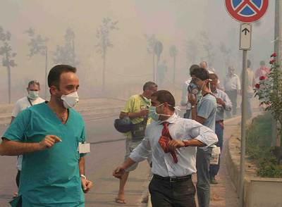 Decenas de personas se protegen del humo con mascarillas al ser evacuadas de un hospital  de Cefalú.