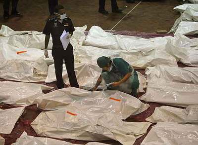 Un policía y un forense examinan los cadáveres de los pasajeros del avión que se estrelló ayer en la isla tailandesa de Phuket.