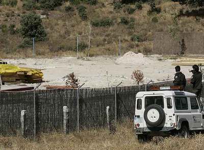 Unos agentes forestales vigilan el interior de una finca desde la valla exterior.
