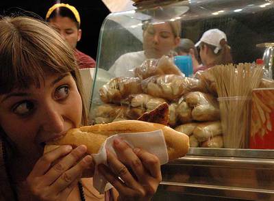 Una joven come un bocadillo en un puesto de comida en la calle.