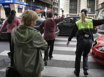 Una viandante cruzó ayer la calle de Guillén de Castro de Valencia indignada por la larga espera y la prioridad al tráfico, mientras un policía intenta para los coches.