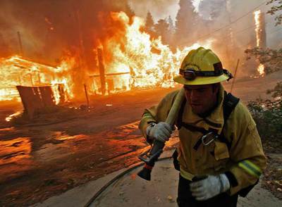 Un bombero arrastra una manguera ante  viviendas en llamas en la localidad californiana de Running Springs
