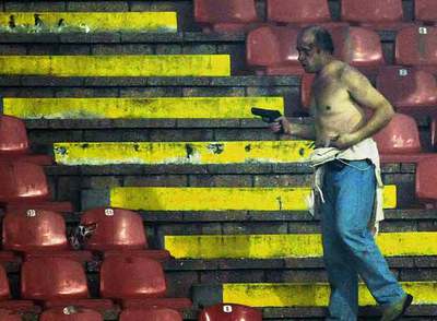 El policía herido por hinchas violentos camina por las gradas empuñando su pistola reglamentaria.