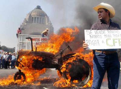 Un agricultor mexicano muestra una pancarta mientras arde un tractor a su espalda, en las protestas en México.