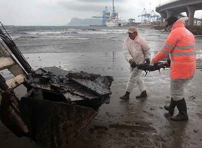 Dos trabajadores recogían ayer desechos procedentes del  New Flame  en la playa de la Concha de Algeciras.