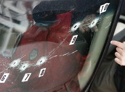 Un agente de  la Ertzaintza observa los impactos de bala en un coche junto al lugar donde fue asesinado ayer Isaías Carrasco, en Mondragón.