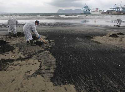 Dos hombres retiran chapapote proveniente del 'New Flame' en la playa del Rinconcillo, en febrero pasado.