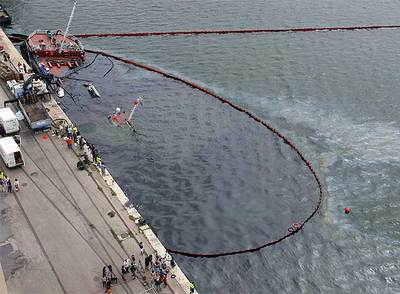 La proa de la gabarra 'Savinosa' asomaba ayer rodeada de manchas de fuel y de una doble barrera de contención.