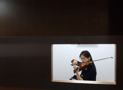Una alumna de la Escuela Superior de Música Reina Sofía practica en una sala de ensayo.  En la puerta, una pantalla indica  quién y cuánto tiempo ocupa la cabina.