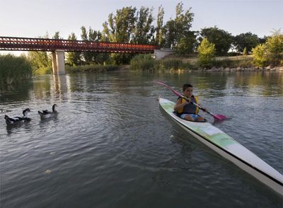 Un niño hace piragüismo en un tramo del Tajo, a su paso por Fuentidueña de Tajo (Cuenca). Al fondo, un puente de finales del XIX.