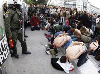 Varios manifestantes simulan ser prisioneros ante los policías antidisturbios que vigilan la sede del Parlamento en Atenas.