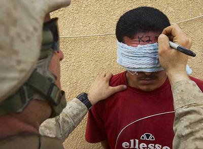 Un  marine  estadounidense rotula un número en la frente de un prisionero, detenido en Haditha (Irak), en mayo de 2005.