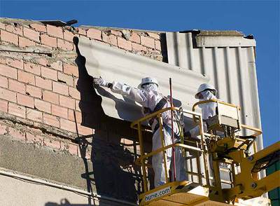 Dos operarios retiran chapas de uralita del techo de la escuela Ferran y Clua del Valldoreix.