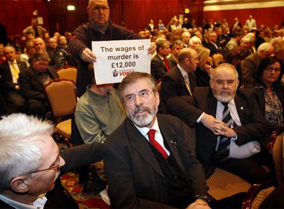 Detrás de Gerry Adams, líder del Sinn Féin, un hombre alza un cartel:  El sueldo del asesino es 12.000 libras. 