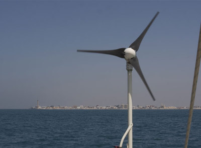 Imagen del pequeño aerogenerador del barco de la organización Oceana, fondeado el pasado miércoles a dos millas de Chipiona. Al fondo, el municipio gaditano.