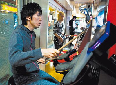  Las recreativas musicales causan furor en Japón desde hace una década. En primer plano, un tokiota aporreando el  Drum mania,  y al fondo, otro jugando al  Guitar freaks.  