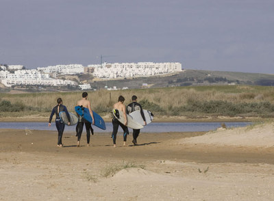 Surfistas pasean frente al paraje de El Palmar donde se proyectan los apartahoteles.