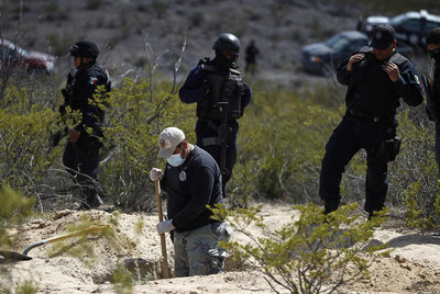 Policías federales protegen el trabajo de un forense en una fosa común.