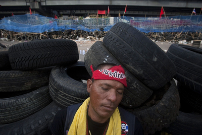 Un  camisa roja  duerme sobre uno de los muros de neumáticos que  la oposición ha utilizado para levantar barricadas en Bangkok.
