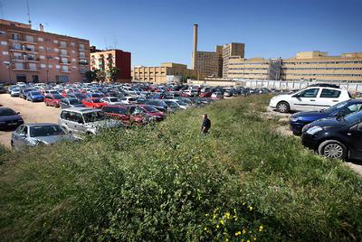 El gran solar del barrio de Tendetes, con los coches aparcados, las hierbas y el hospital La Fe  al fondo.