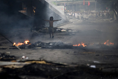 Un miembro de los  camisas rojas  camina a través del humo y el fuego en una calle céntrica de Bangkok.