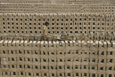 Un niño transporta arcilla para hacer ladrillos a mano en Calcuta (India). El trabajo infantil nutre a grandes empresas.