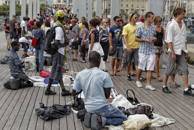Un grupo de  manteros  vende bolsos y abanicos en La Rambla del Mar en Barcelona.