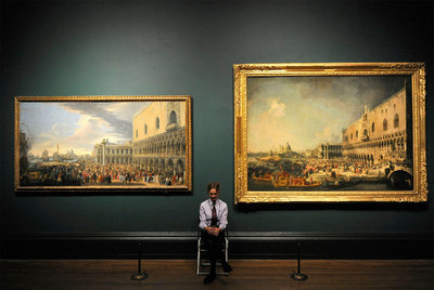 Una guarda de seguridad de la National Gallery, entre un paisaje de Luca Carlevarijs (izquierda) y otro de Canaletto.